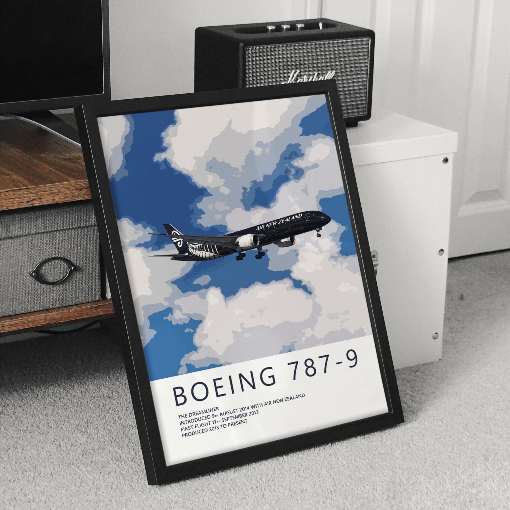 A framed poster of a Boeing 787-9 airplane flying in the sky, with a text overlay that reads "BOEING 787-9" and "AIR NEW ZEALAND".